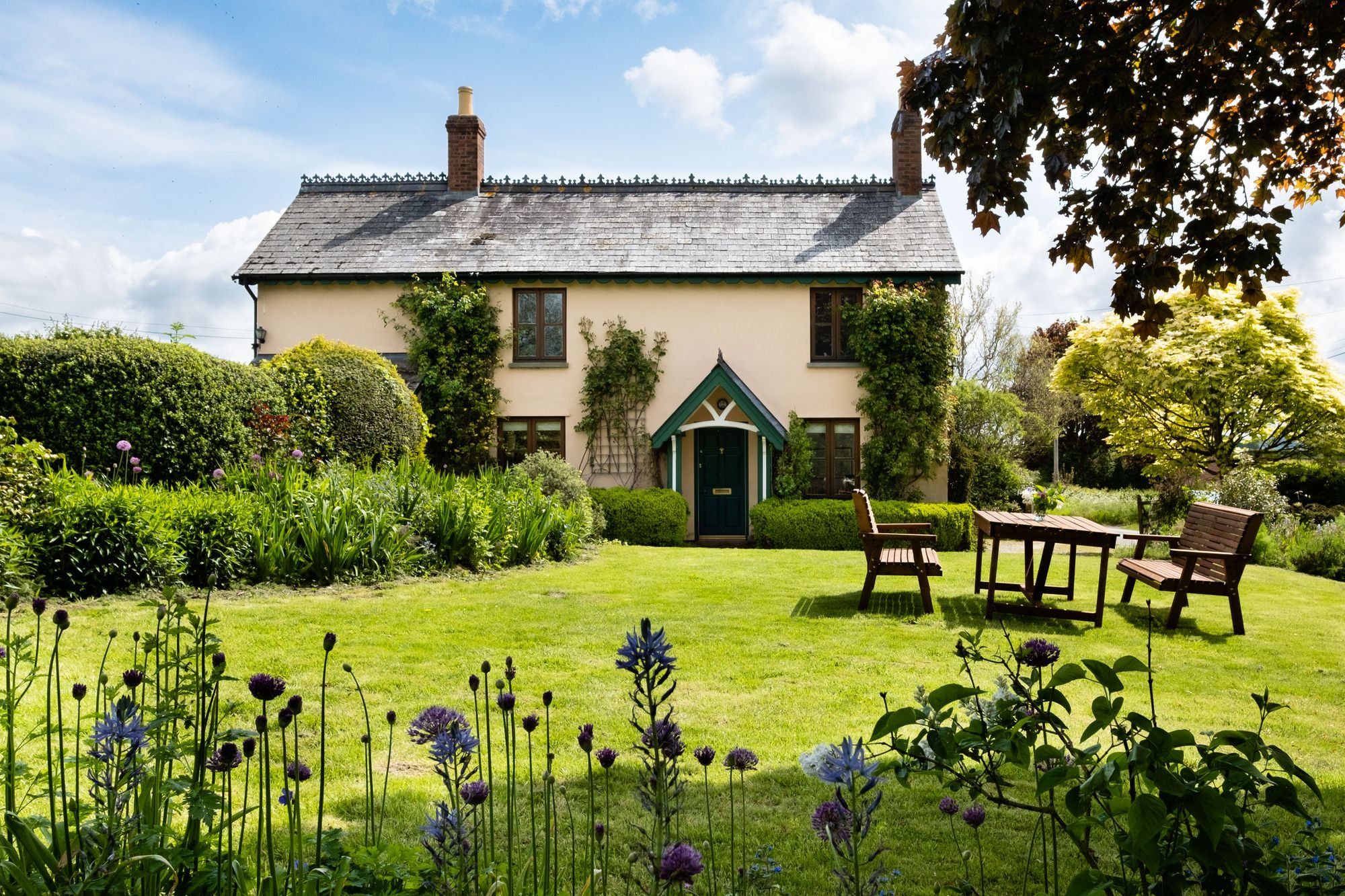 A white cottage behind a neat lawn and planted borders on a sunny day