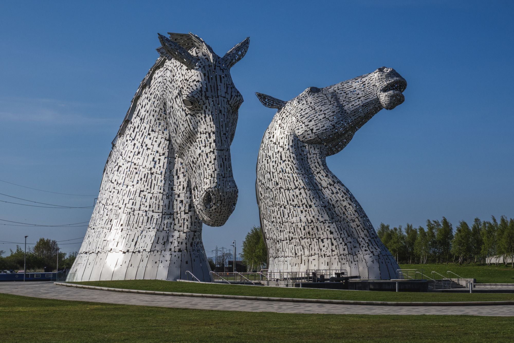 The Kelpies, two giant steel horse head sculptures near Falkirk, against a clear blue sky with grass and a path in front