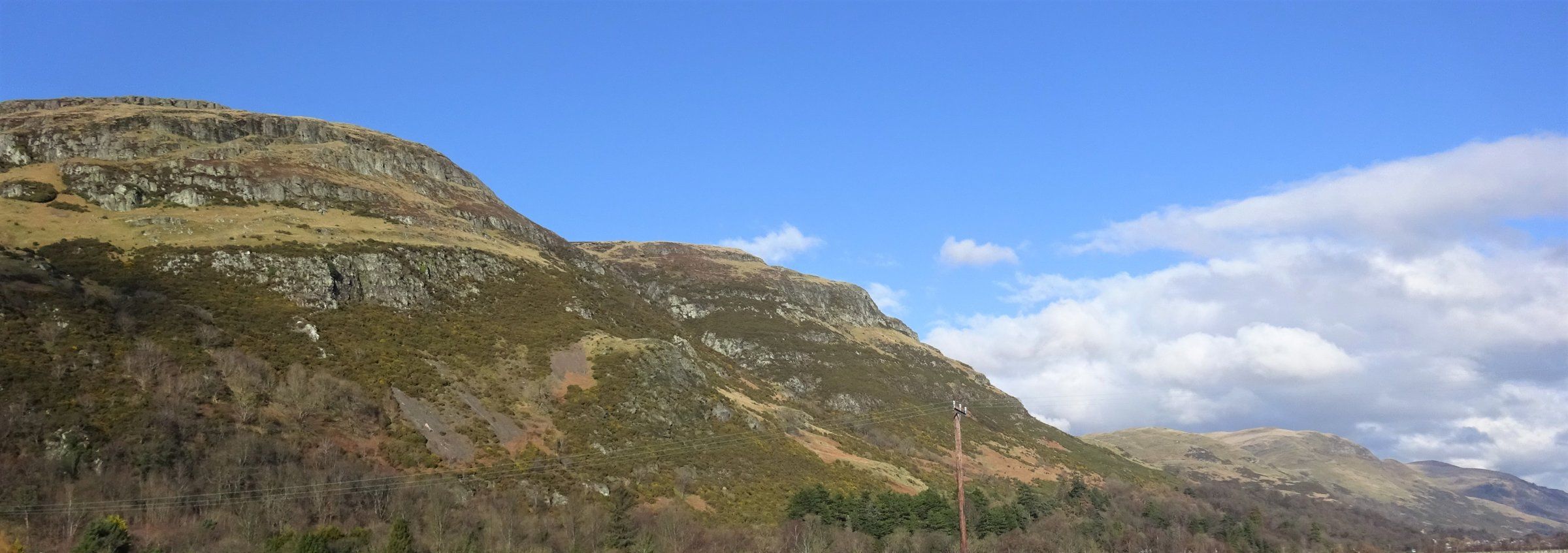 The craggy southern face of the Ochil Hills seen from Blair Mains near Clackmannan, under a blue sky