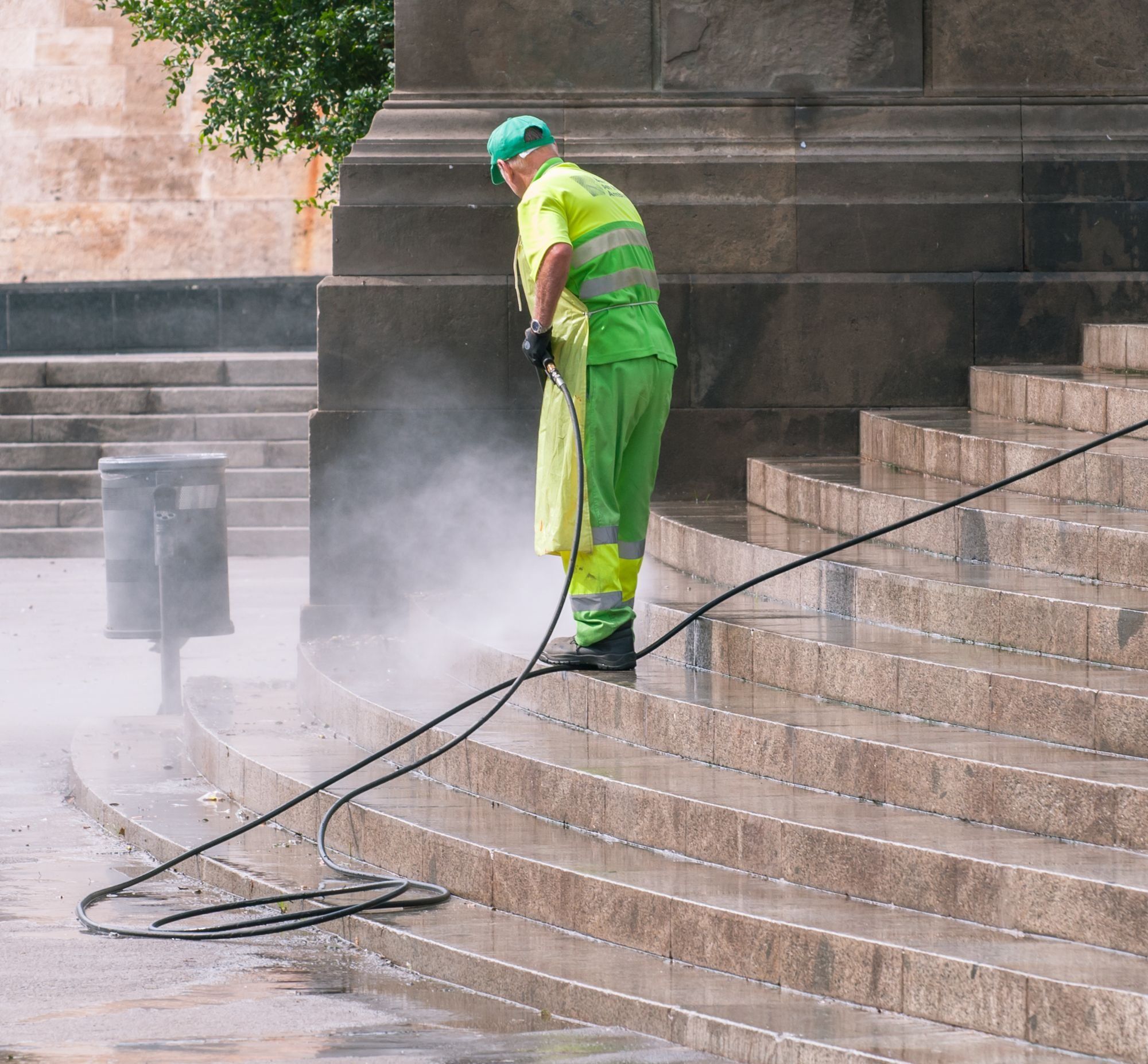 An operative in high-visibility clothing pressure washing a wide flight of stone steps, with spray rising off the wet stone