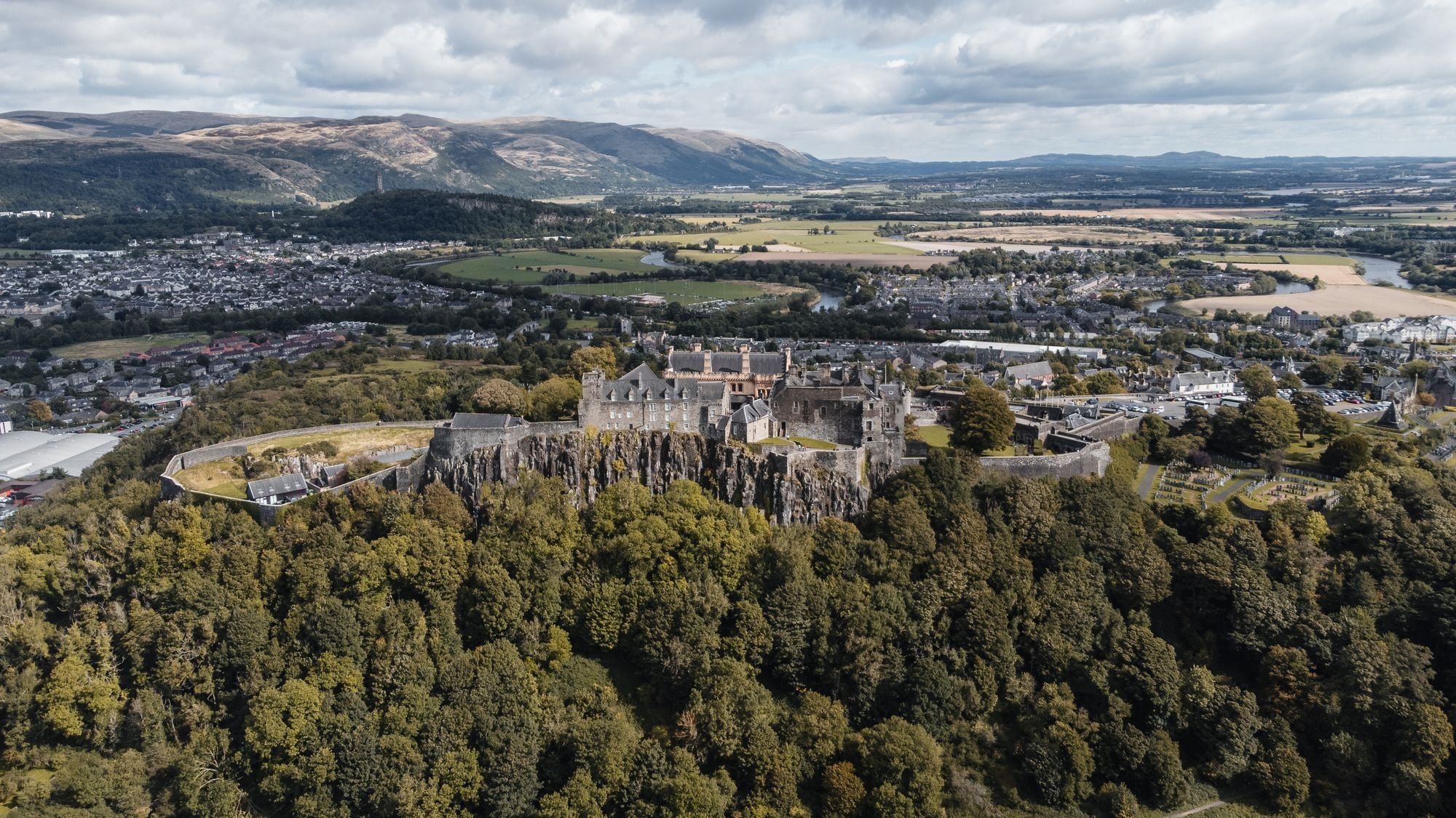 Aerial view of Stirling Castle on its wooded crag, with the town, the winding River Forth and the Ochil Hills beyond